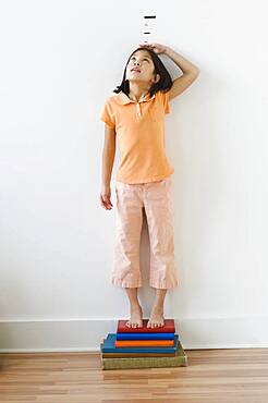 Asian girl standing on books in front of height markers