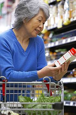 Senior Asian woman reading label at grocery store