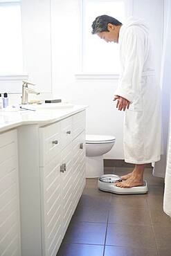 Asian man standing on bathroom scale