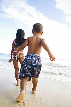 Pacific Islander siblings running on beach