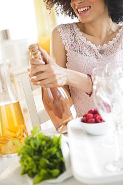 Mixed race woman opening bottle of wine