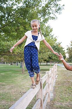 Father helping daughter balance on wooden fence