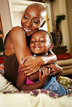 Black mother and daughter hugging on sofa