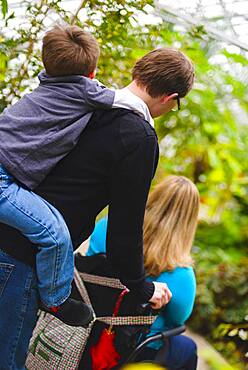 Man pushing paraplegic wife and carrying son piggyback