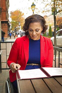 Disabled woman in wheelchair reading menu at sidewalk cafe