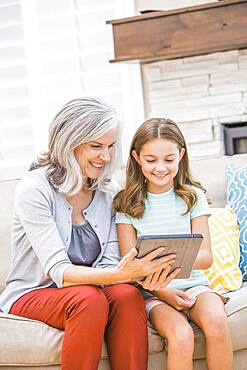 Caucasian grandmother and granddaughter using digital tablet on sofa