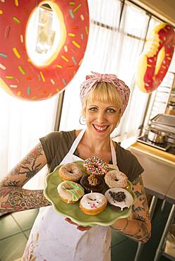 Asian baker holding plate of donuts in bakery