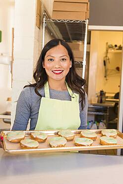 Asian baker holding tray of donuts in bakery