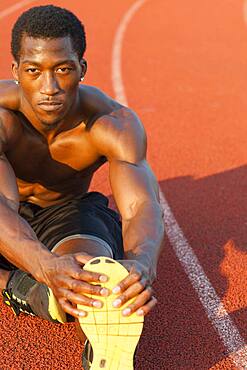 Black athlete stretching on track in sports field