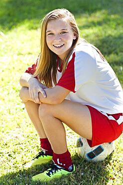 Caucasian soccer player sitting on ball in grass,