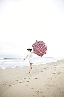 Woman walking in wind with umbrella on beach