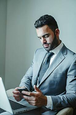 Businessman using laptop and cell phone in armchair