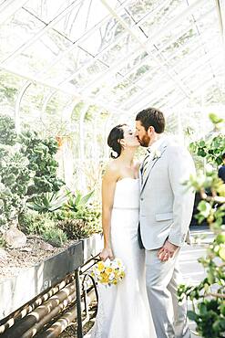 Caucasian bride and groom kissing in greenhouse