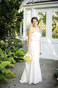 Caucasian bride holding bouquet in garden