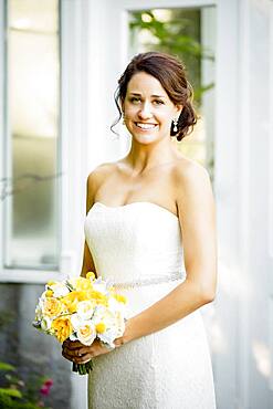 Caucasian bride holding bouquet in garden