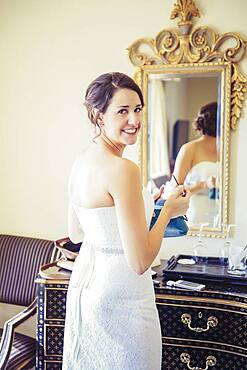 Caucasian bride applying makeup in mirror