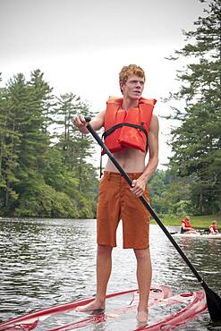 Caucasian teenage boy rowing paddleboat in lake