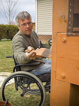 Caucasian paraplegic man painting deck in backyard