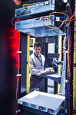 Hispanic technician using computer in server room