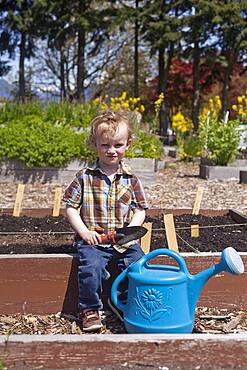 Caucasian boy holding spade with watering can in garden