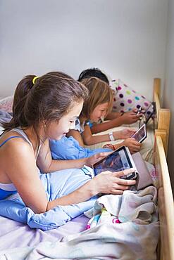 Girls using digital tablets on bed