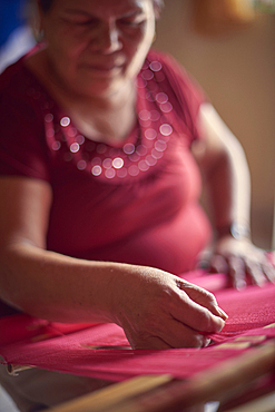 Hispanic woman weaving fabric on loom