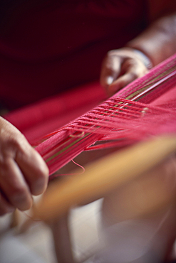 Hispanic woman weaving fabric on loom