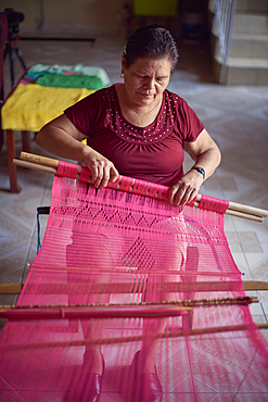 Hispanic woman weaving fabric on loom