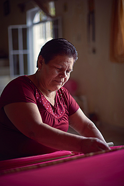 Hispanic woman weaving fabric on loom