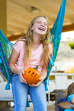 Laughing Caucasian girl in hammock holding pumpkin