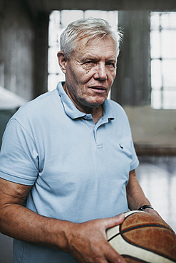 Portrait of serious Caucasian man holding basketball in gymnasium