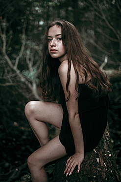 Serious Caucasian woman sitting on log in forest