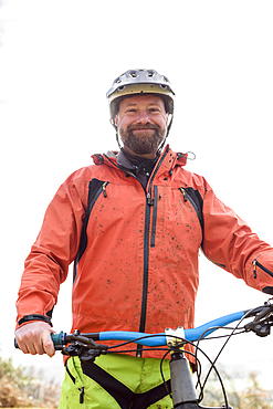 Portrait of smiling Caucasian man splattered in mud holding bicycle