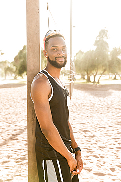 Portrait of smiling black man leaning on beach volleyball net