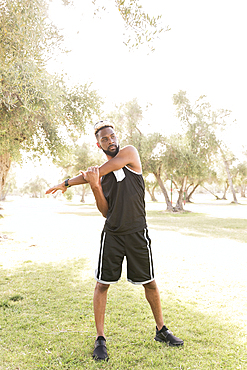 Black man standing in park stretching arm