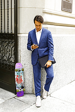 Caucasian businessman with skateboard texting on cell phone