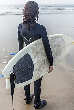 Caucasian woman standing on beach holding surfboard