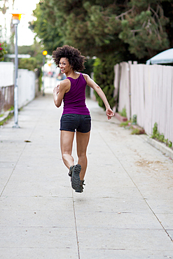 Smiling Mixed Race woman running on sidewalk