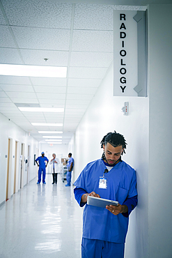 Nurse leaning on wall in hospital using digital tablet