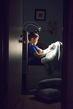 Caucasian boy reading book in bed at night