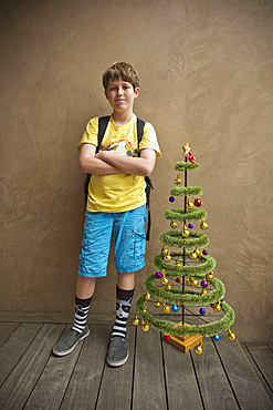 Portrait of Caucasian boy standing near small artificial Christmas tree