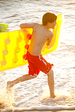 Caucasian boy running into ocean carrying inflatable raft