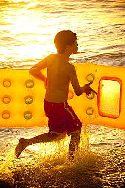 Caucasian boy running into ocean carrying inflatable raft