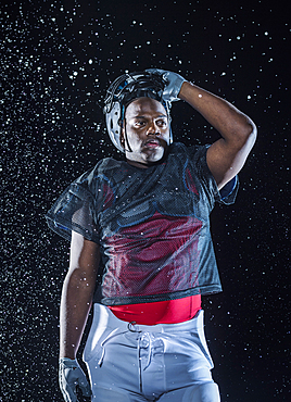 Water splashing on Black football player lifting helmet