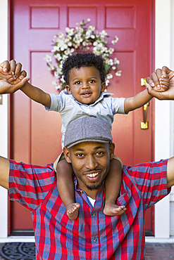 Smiling mixed race father carrying baby son on shoulders