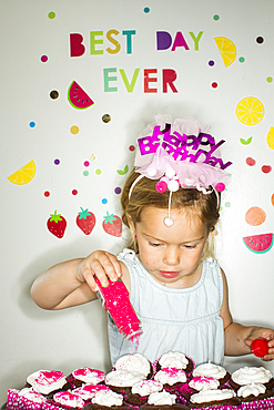 Caucasian girl sprinkling sprinkles on tray of cupcakes for birthday