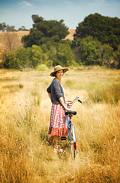 Portrait of smiling Caucasian woman standing in field with bicycle