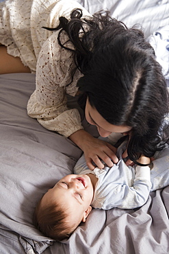 Caucasian mother laying on bed tickling baby son