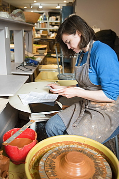 Caucasian woman reading paperwork near pottery wheel