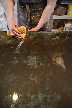 Caucasian woman wiping workshop table with wet sponge